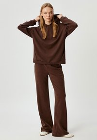 Brown hoodie met een relaxte pasvorm en verstelbare trekkoorden, gecombineerd met bijpassende wijdvallende joggingsbroek, gemaakt van zachte stof.