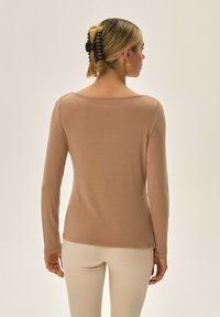 Długi rękaw w beżowym materiale, z szerokim dekoltem i dopasowanym krojem. Gładka tekstura i uproszczona sylwetka. Ukryte detale szwów.