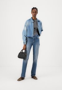 Chaqueta de mezclilla, top gris, jeans azul claro, bailarinas de estampado de leopardo; sosteniendo un pequeño bolso negro con superficie texturizada y acentos.