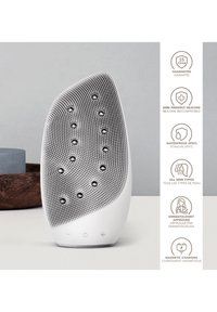 Vit silikon ansiktsrengöringsanordning med texturerat mönster och knappar för justeringar. Vattentät design med en magnetisk laddningsfunktion.