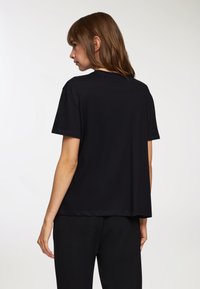 T-shirt nera in cotone con maniche corte, una vestibilità morbida e scollo rotondo. Design semplice, texture morbida e nessun motivo o accento visibile.