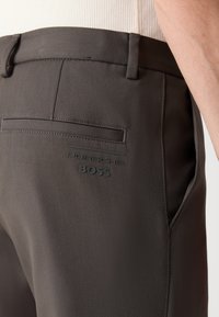 Gray tailored trousers with a smooth texture, featuring a back pocket and subtle branding reading “Porsche BOSS” in black.