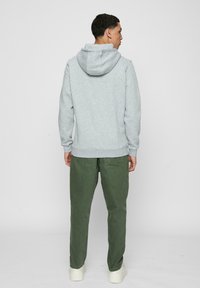 Grå hettegenser med stor hette, kombinert med olivengrønne bukser og hvite sneakers. Hettegenseren har ribbestrikkede mansjetter og nedkant, laget av mykt stoff.