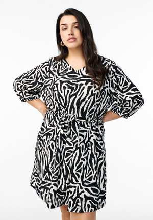 Vestido en blanco y negro con un patrón similar al de una cebra, con escote en V, mangas cortas y un cinturón de tela en la cintura. Material texturizado.