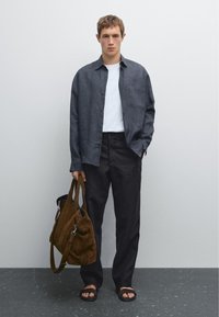 Button-up dark gray linen shirt over a white t-shirt, paired with pinstriped pants. Brown suede bag and sandals complete the look.