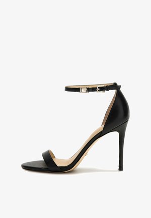 Sandalo alto nero con tacco, con una sottile cinghia alla caviglia, punta aperta, materiale in pelle e design a punta. Dettaglio della fibbia in tono dorato.