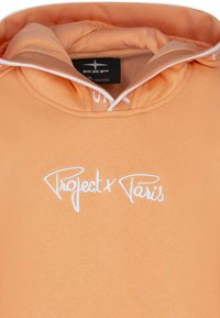 Hoodie orange avec un cordon de serrage et un logo brodé blanc "Project x Paris" à l'avant. Texture de tissu lisse avec capuche intégrée.