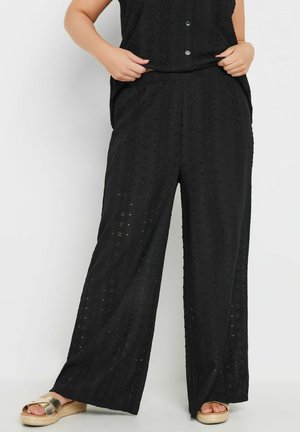 Zwarte wijde leg pantalons met een gestructureerd ontwerp en uitsnijdingen, gemaakt van lichte stof. Gestyled met een bijpassende top en sandalen.