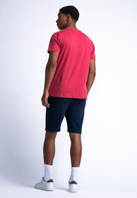 Červené tričko s krátkým rukávem a kulatým výstřihem, spárované s námořnickými šortkami, bílými kotníkovými ponožkami a bílými teniskami se zeleným akcentem.