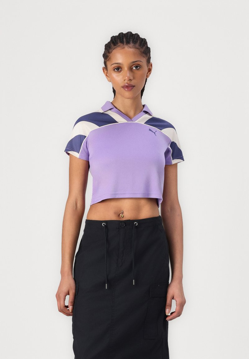 Polo crop em roxo com colarinho, apresentando padrões curvos em azul escuro e creme. S saia cargo preta com bolsos laterais e cordão.