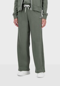Pantaloni sportivi verdi realizzati in materiale morbido, con vita regolabile con cordino e un accento di logo bianco. Il design è a vestibilità ampia e a lunghezza completa.