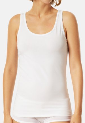 Woman wearing a plain white sleeveless tank top and white underwear, with a neutral background.