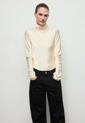 Top de cuello alto color crema hecho de una tela suave, combinado con jeans de pierna ancha negros de cintura alta, que cuentan con bolsillos frontales y cierre de botón.