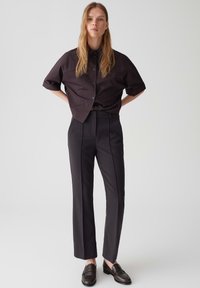 Chemise à manches courtes, sombre, à boutons, associée à un pantalon noir slim taille haute et des mocassins sombres ; tissu lisse et design ajusté.