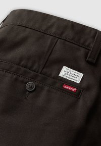 Close-up of dark brown Levi’s pants back pocket with black button and two white and red Levi’s brand labels.