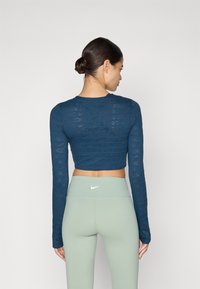 Sötétkék, hosszú ujjú, cropped felső, finom Nike logó mintával, párosítva világos zöld, magas derekú leggings-szel, kicsi fehér logóval.