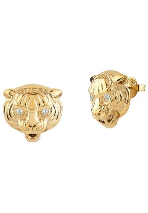 Boucles d'oreilles en ton doré présentant un design détaillé de tête de tigre avec des yeux étincelants et un logo "GUESS" gravé, offrant une finition texturée.