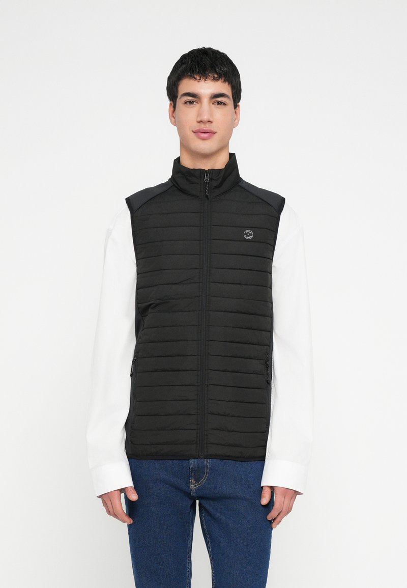 Čierna prešívaná vesta s vysokým golierom, predným zipsom a bočnými vreckami. Má logo na hrudi a textúrované panely na pleciach.