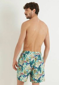 Les short de bain pour hommes présentent un motif floral avec des teintes vertes, bleues et roses. La taille est élastique, offrant un ajustement confortable.