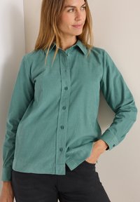 Chemise boutonnée teal en tissu léger avec un col structuré et des manches longues. Présente un ourlet droit et des boutons assortis.