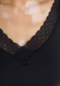 Black top featuring a scalloped lace V-neckline. The texture is smooth, with a light sheen, complemented by intricate lace detailing.