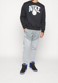 Svart sweatshirt med "NIKE" i stor vit text, grå sweatpants med sidostråkar, och svarta sneakers med blå detaljer.