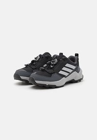 Black and gray athletic shoes with a textured mesh upper, rubber sole, lacing system, and three distinctive white stripes on the side.