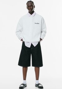 Hvid sweatshirt med broderi af "Fresh Codes", lagd over en pink stribet skjorte. Sorte denim shorts og sorte slip-on sko med hvide sokker.