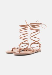 Tan lederen sandalen met spiraalvormige veters en platte zolen. Kenmerkt zich door slanke banden en een minimalistisch ontwerp, dat de natuurlijke textuur van het materiaal accentueert.