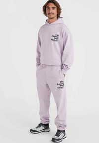 Lichtpaarse hoodie en sweatpants met "The Future Surf Society" in het zwart gedrukt. Zacht materiaal, relaxte pasvorm en ribbelmanschetten.