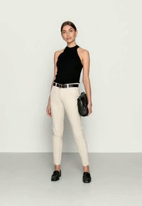 Top preto de gola alta sem mangas combinado com calças creme de corte justo, uma bolsa preta e loafers pretos; estilo minimalista com um ajuste moderado.