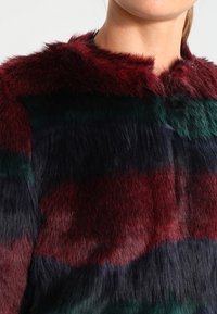 Faux fur coat with a striped pattern in burgundy, green, and navy. Features a high collar and soft, textured surface.