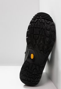 Suela de zapato exterior negra con un patrón de relieve resistente. Presenta un logo de Vibram amarillo y acentos texturizados para un mejor agarre.