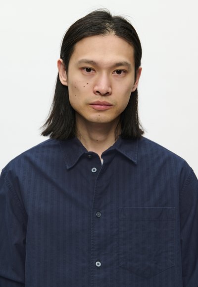 Camisa de botones azul marino con textura a rayas, con cuello, mangas largas y un bolsillo en el pecho. Hecha de tela ligera.