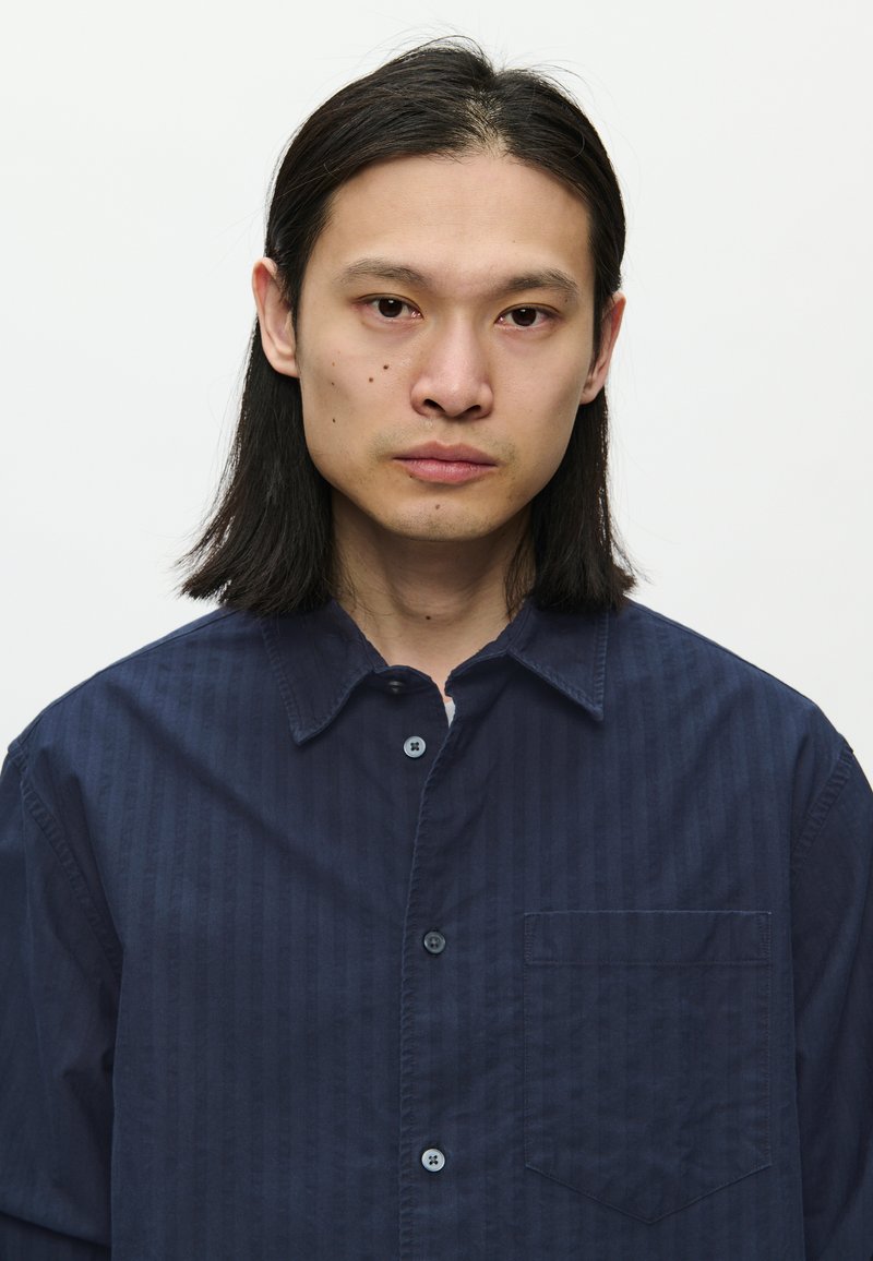 Navyblaues Button-down-Hemd mit Streifenstruktur, ausgestattet mit einem Kragen, langen Ärmeln und einer Brusttasche. Hergestellt aus leichtem Stoff.