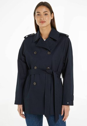 Trench coat doppiopetto blu navy con vita cintata, grandi bottoni, moschettone sulle spalle e maniche lunghe. Tessuto liscio, vestibilità casual.