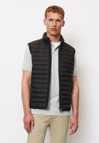 Schwarze, gesteppte Weste mit hohem Kragen, Reißverschluss und Seitentaschen, getragen über einem hellgrauen Poloshirt mit glatter, matter Textur.