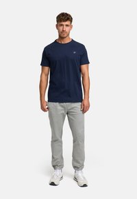 Granatowa bawełniana koszulka z okrągłym dekoltem, w zestawie z jasnoszarymi spodniami z elastycznym dołem i białymi butami sportowymi.