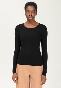 Schwarzer gerippter Langarmpullover mit rundem Ausschnitt. Weiche Textur und figurbetontes Design, kombiniert mit beigen weit geschnittenen Hosen.