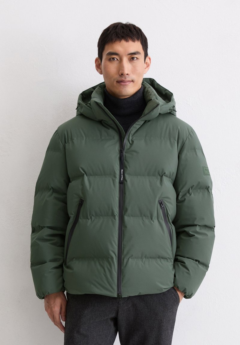 Veste puffer verte avec capuche, design matelassé, fermeture éclair à l'avant et deux poches latérales. Conçue en matériau lisse et résistant à l'eau.