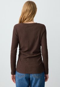 Bruine lange mouwen top met een gestructureerde stof, ronde halslijn en een getailleerde pasvorm, gecombineerd met hoog-getailleerde blauwe jeans.