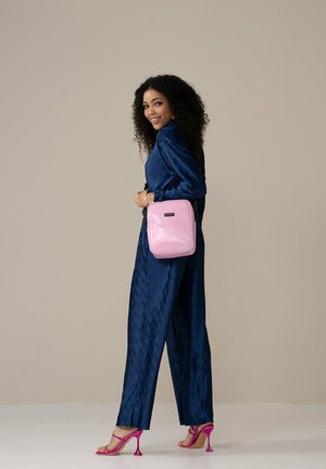Blaues geripptes Jumpsuit, pinke glänzende quadratische Tasche mit strukturierten Oberflächen und durchsichtige pinke High-Heelsandalen. Schlichtes und modernes Design.