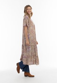 Maxi kjole med paisley mønster i varme nuancer. Letvægtsstof, korte ærmer og lagdelt design. Kombineret med mørke flared jeans og brune støvler.
