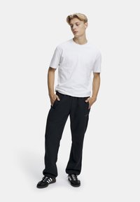 Hvit bomull t-skjorte kombinert med løstsittende svarte joggebukser, med sidelommer og logodetaljer. Svarte joggesko med hvite striper.