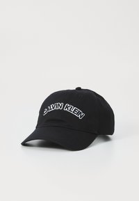 Čierna baseballová čiapka vyrobená z bavlny, s bielym vyšívaným textom "CALVIN KLEIN" na prednej strane a zakriveným šiltom.