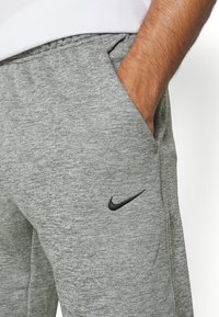 Grå atletiska joggers i texturerad tyg, med elastisk midja, sidofickor och en svart Nike-logotyp på låret.