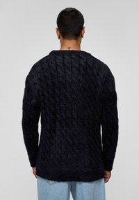 Donkerblauwe gestructureerde trui met een kabelbreipatroon, met lange mouwen en een ontspannen pasvorm. Zacht materiaal, zoom op heuphoogte.
