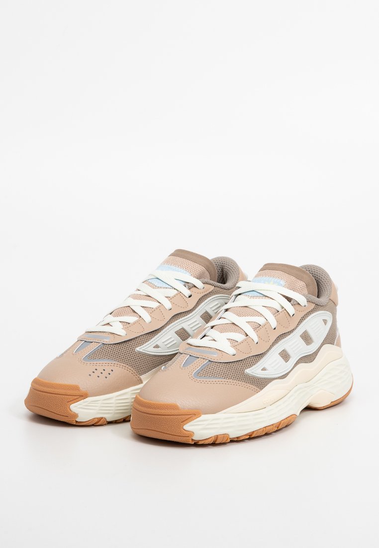 Sneaker in rete beige e grigio con accenti bianchi, superfici testurizzate e una spessa suola intermedia bianca. Presentano lacci bianchi e suole in gomma.