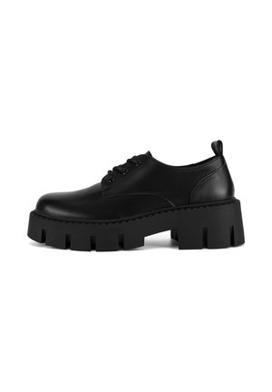 Zapatos de cuero negros con punta redondeada, diseño de cordones, suela gruesa de plataforma y un patrón de banda de rodadura chunky distintivo. Presenta una lengüeta en la parte posterior.