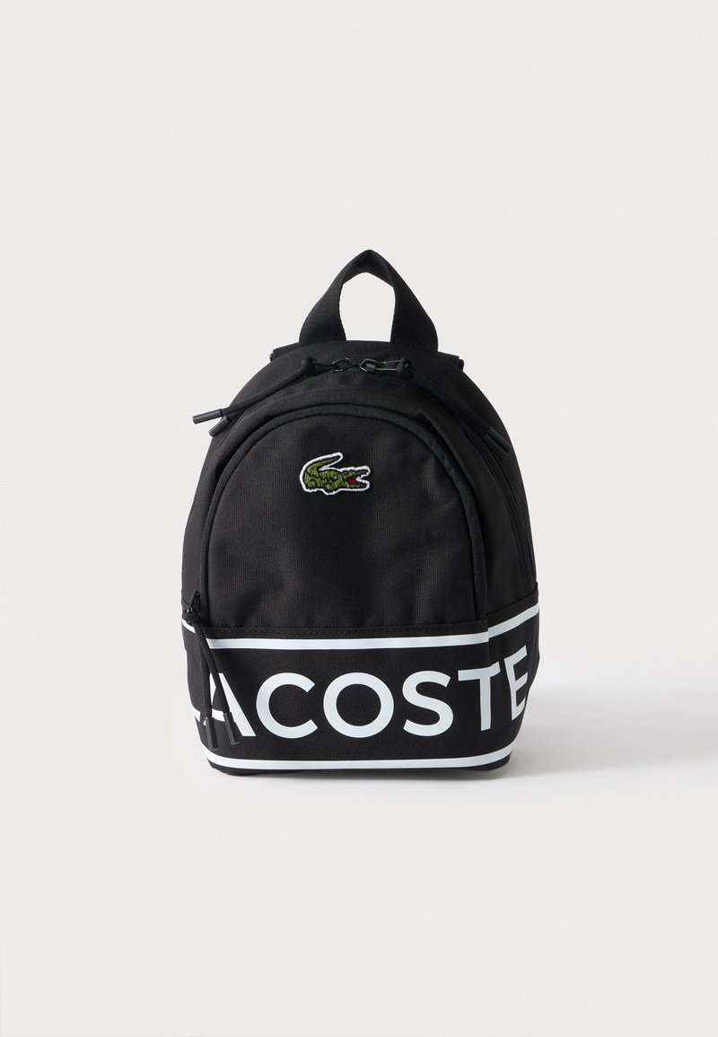 Μαύρο σακίδιο πλάτης Lacoste με μπροστινή τσέπη με φερμουάρ, πράσινο λογότυπο κροκόδειλου και μεγάλο λευκό κείμενο Lacoste στο κάτω τμήμα.